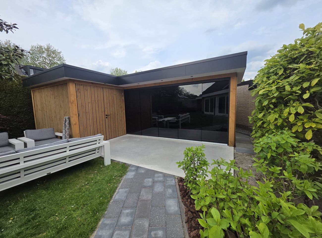 Moderne tuinkamer met houten lattenwerk en glazen schuifpui, gebouwd als overkapping